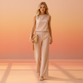 Woman wearing a pink sleeveless top and pants with a beige clutch against a beige background